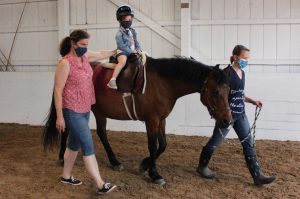 Preschooler rides pony while one adult leads the horse and another adult supports the student.