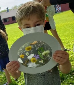 Preschooler holds a project made up of a cardboard circle, a translucent contact paper center with flowers and leaves placed on it.